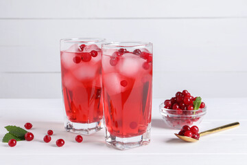 Tasty cranberry juice with ice cubes in glasses and fresh berries on white wooden table