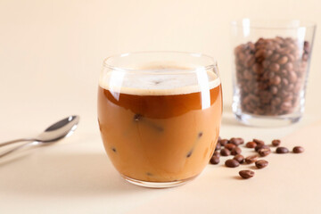 Refreshing iced coffee with milk in glass and beans on beige background