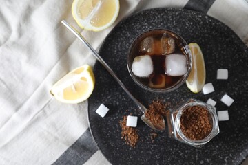 Refreshing iced coffee in glass, sugar cubes, lemon and spoon on cloth, top view