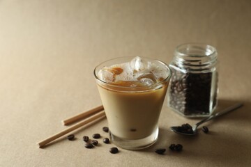 Refreshing iced coffee with milk in glass, straws and beans on beige background, closeup