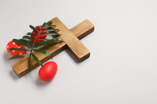 Wooden cross, painted Easter eggs and palm leaf on light grey background, space for text