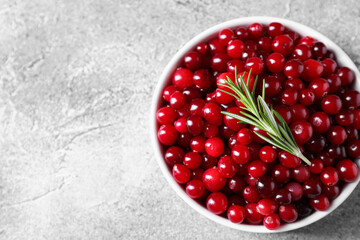Fresh ripe cranberries and rosemary in bowl on grey table, top view. Space for text