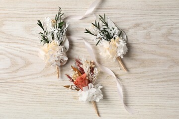 Stylish boutonnieres on white wooden table, flat lay