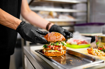 chef hand cooking cheeseburger with vegetables and meat on restaurant kitchen