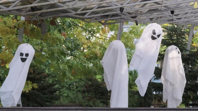 White ghost decorations hanging on roof near green trees in park during Halloween