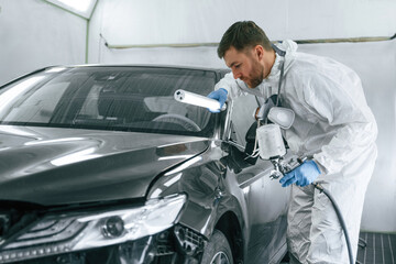 By help of lighting equipment. Man is painting a car by using spray guy