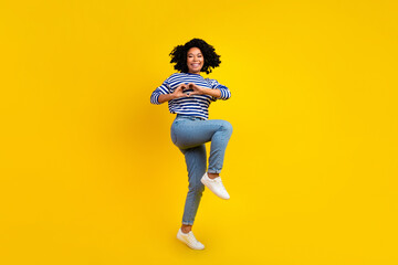 Full size photo of lovely appreciative woman dressed striped shirt flying showing heart on chest isolated on yellow color background