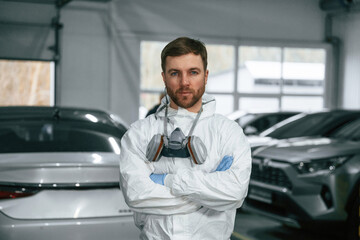 Portrait of professional painter with mask that is standing in the garage with cars