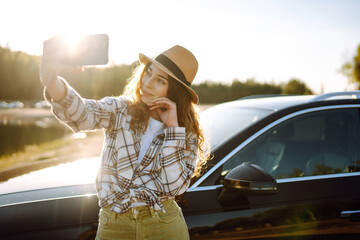 Happy woman on vacation taking selfie photo with smartphone near car. Stylish model on a car trip....