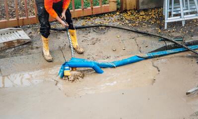 A worker repairs a broken water pipe on the street by using a pump to empty the trench. - 742857120