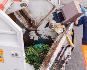 Ecological worker empties bucket of organic waste into garbage truck.