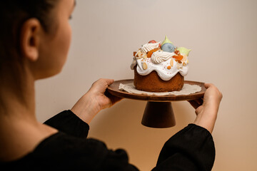 Baker in a black dress turns his back to the camera and holds a beautifully decorated Easter cake on a stand
