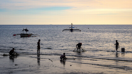 Fototapeta na wymiar Silhouettes of fishermen and wooden fishing boats against the backdrop of a beautiful sea horizon with sunset, seascape in pastel colors