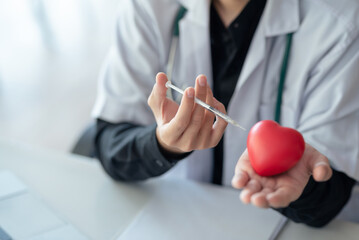 Healthcare worker with syringe and red heart model. Health, love, and cardiology concept.