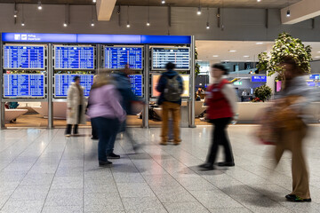 People in motion blur walking along in front of a departure scoreboard in the Frankfurt International Airport