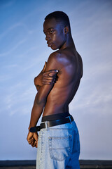 shirtless african american man in stylish jeans posing on blue watery backdrop and looking away