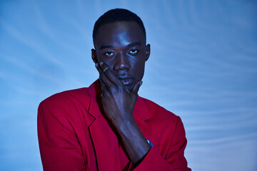 fashionable young african american man in red vibrant blazer posing on blue watery background
