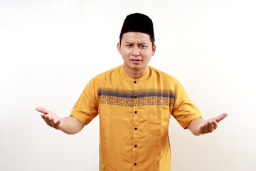 Confused Asian muslim man in koko shirt with skullcap spreading his hands