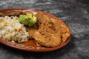 Breaded fried fish and rice in a clay dish on a wooden table.