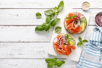 Salmon sandwiches with bagel, salted fish, fresh cucumber, onion and basil on white background, top view. Healthy breakfast with salmon toasts - 742905958