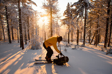 Male skier stands against huge fir trees covered with snow and puts his backpack from snow