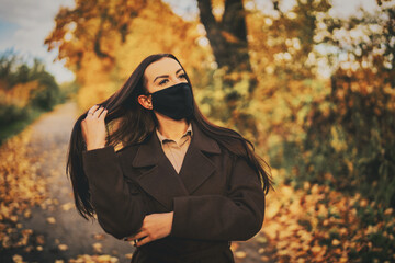 Portrait of a young woman with black mouth mask in a brown coat in autumn
