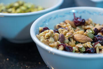 White bowl on black marble background full multi types of nuts and dried fruits like cherries and grape