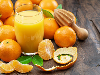 Obraz na płótnie Canvas Orange tangerine fruits and glass of fresh tangerine juice on dark wooden background. Top view.