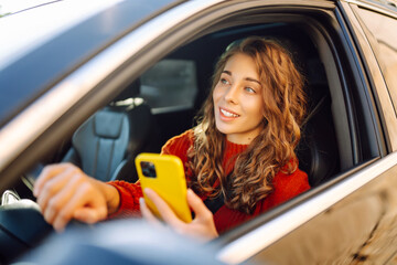 Young woman driver sitting in car, using smartphone. Checking email chats and reading news. Concept...