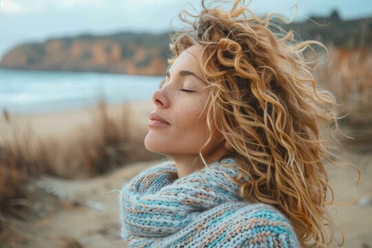 A free-spirited woman embraces the winter beach with her wild curls and warm scarf, gazing up at the endless sky while her surfer hair dances in the wind