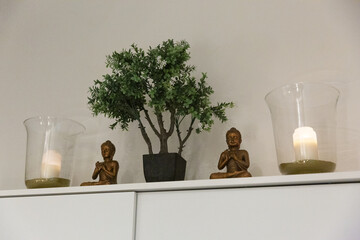 Buddha statue on a white shelf with candles and a tree.