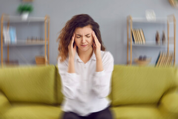 Woman feels dizzy and sits down on the couch. Young woman sitting on the sofa at home, feeling pain and a spinning sensation in her head. Concept of headache, vertigo, health problem, brain tumor - obrazy, fototapety, plakaty