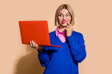 Portrait of minded creative company agent finger touch chin bite lips use laptop isolated on beige...
