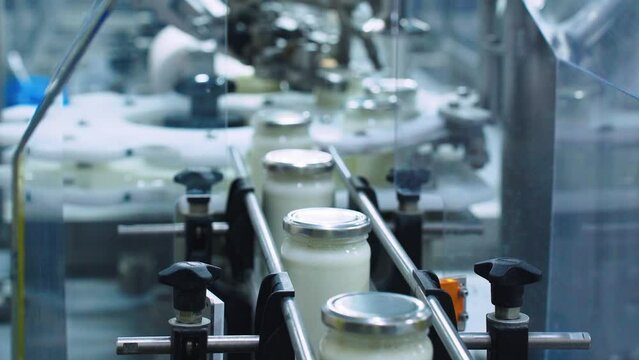 Automatic line for bottling and preserving dairy products at a food factory, close-up. The machine automatically seals lids on milk cans, which then move along a conveyor belt to the warehouse.