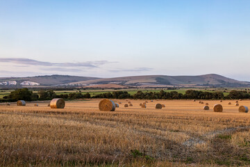 A view over farmland in Sussex with straw bales in a field, and the South Downs hills in the...