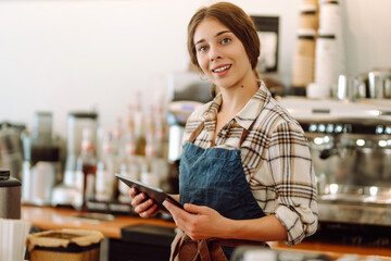 Smiling female barista takes an order from a tablet while standing at the bar counter in a coffee shop. Online order. Small business, people, takeaway and service concept.