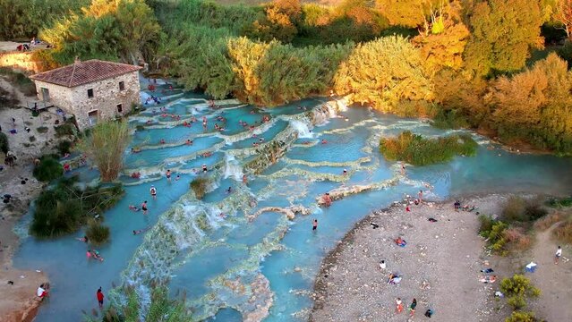 Italy Tuscany Saturnia thermal springs at sunset 4K drone. People in turquoise pools. Scenic Cascate del Mulino golden hour. Luxury wellness travel footage