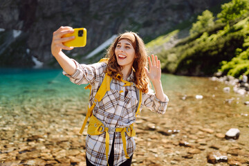Young woman with mountains and lake in background taking selfie.Selfie while traveling. Lifestyle, adventure, nature, active life.