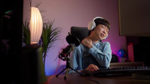 Gaming overtime tired of young Asian women. Stressed gamer female suffering from a neck contracture while sitting at home while live streaming. Neon lights, 4k video footage