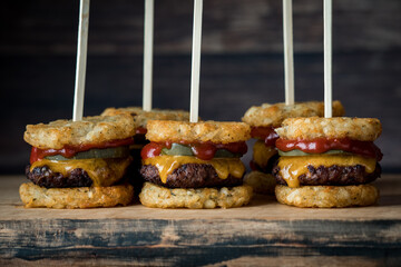 Tater and beef appetizer skewers on a wooden board, against a dark background.