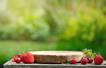 Empty wooden podium stand for cosmetics with fresh berries in a summer garden. Mock up. Wooden...
