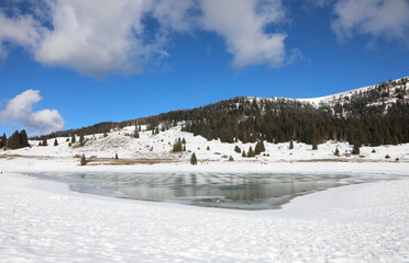 frozen mountain lake in winter with snow and white clouds - obrazy, fototapety, plakaty
