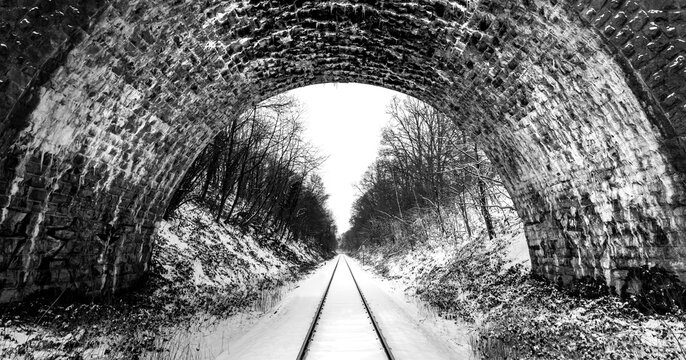 Old brick stone arch bridge spanning over a branch line railway track Iserlohn, Sauerland Germany on cold snowy winter day. Symmetrical panoramic wide angle perspective, black and white grey scale.