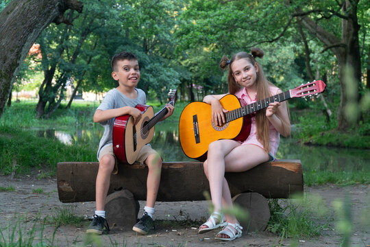 a girl in pink clothes with long hair sits on a bench and plays the guitar, a brunette boy looks at the girl and learns to play the guitar