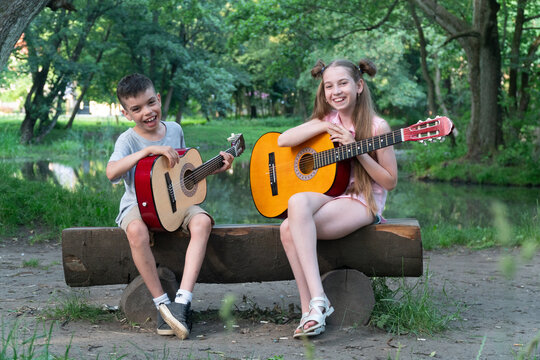 a girl in pink clothes with long hair sits on a bench and plays the guitar, a brunette boy looks at the girl and learns to play the guitar