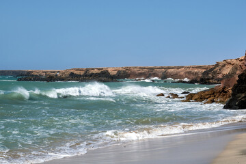 The Atlantic Ocean in Jandia with clear sky and mountains in the back and waves breaking on the...