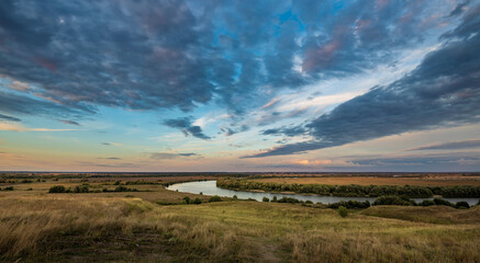 Panorama of rural landscape with river and sunset, dramatic sky