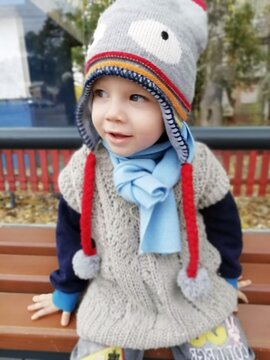 Happy toddler in woolen cap and scarf sitting on bench