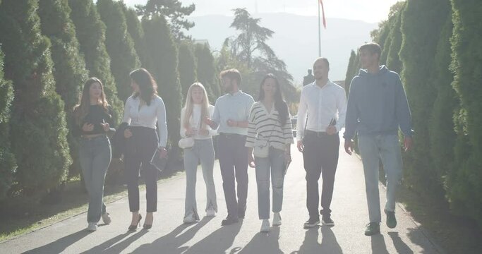 University students relish a leisurely stroll in a sunlit park, engaging in conversations from school life and exams to casual topics, fostering a connection and sharing positivity.