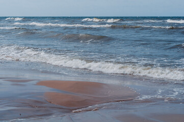 Seascape on Baltic Sea. Foaming waves running towards shore are depicted. Sandy shore is decorated with delicate traces of water, creating  natural pattern.